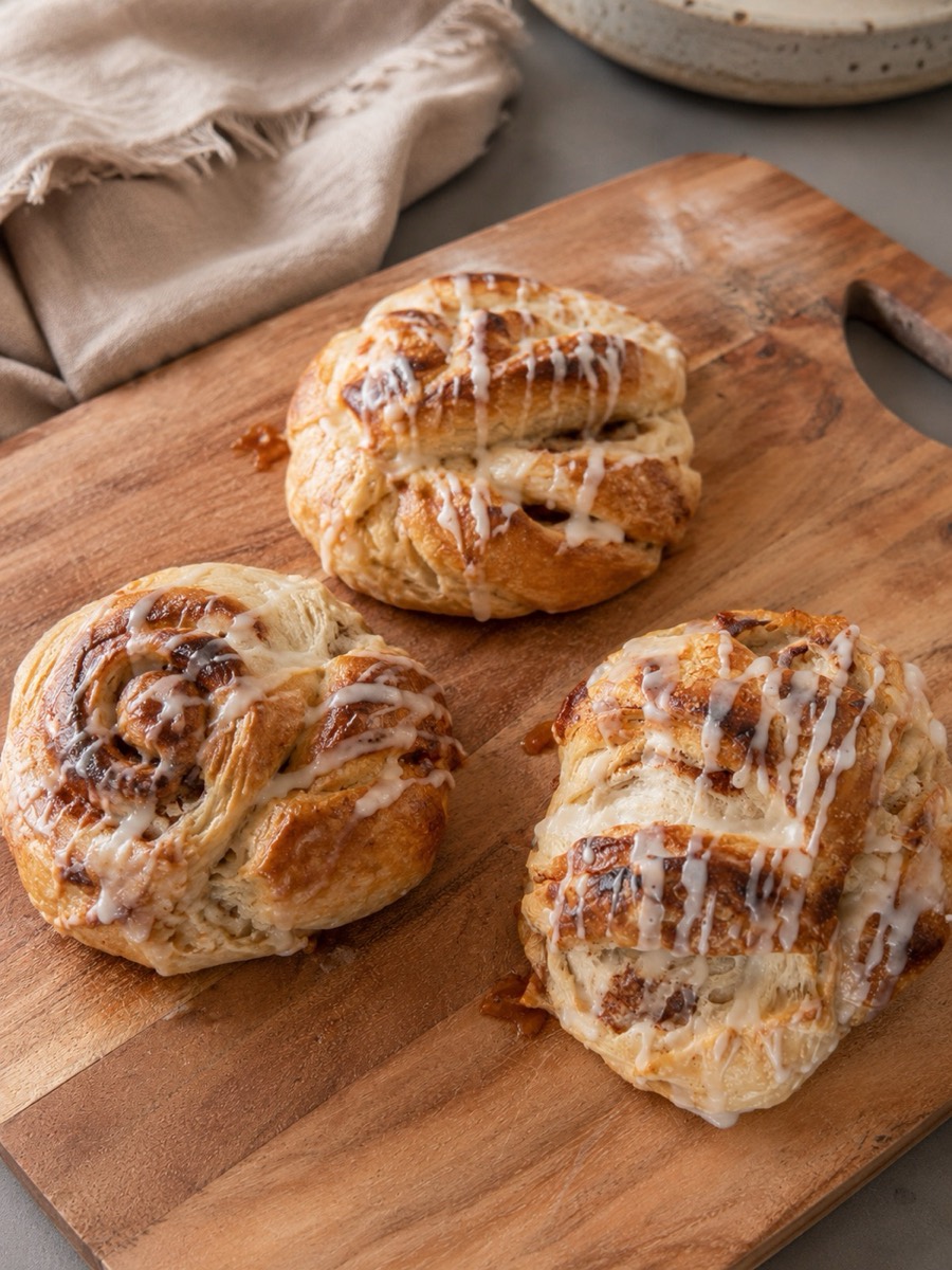 Three glazed cinnamon roll croissant sourdough minis on a wooden board